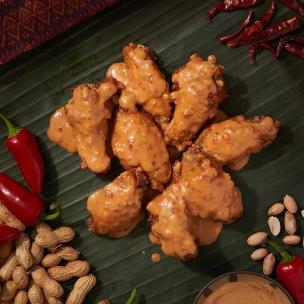 Shlap Muan chicken wings with peanut sauce, peanuts, and red chili peppers on a banana leaf.