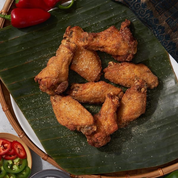 Crispy Shlap Muan chicken wings, seasoned with spices, served on a banana leaf with peppers.