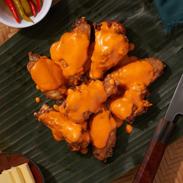 Shlap Muan chicken wings covered in orange sauce, served on a banana leaf with pickled peppers.