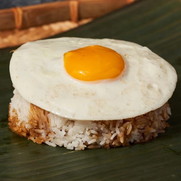 Fried egg with a bright yellow yolk on a bed of white and brown rice, served on a banana leaf.
