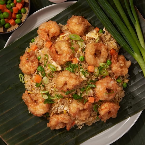 Fried shrimp and rice with peas, carrots, and scallions, served on a banana leaf.