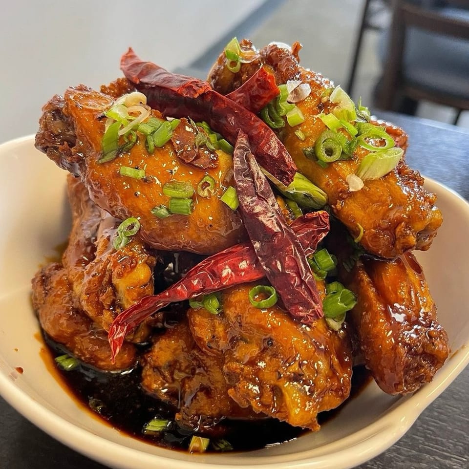 Sweet and spicy chicken wings, garnished with dried red chilies and chopped green onions.