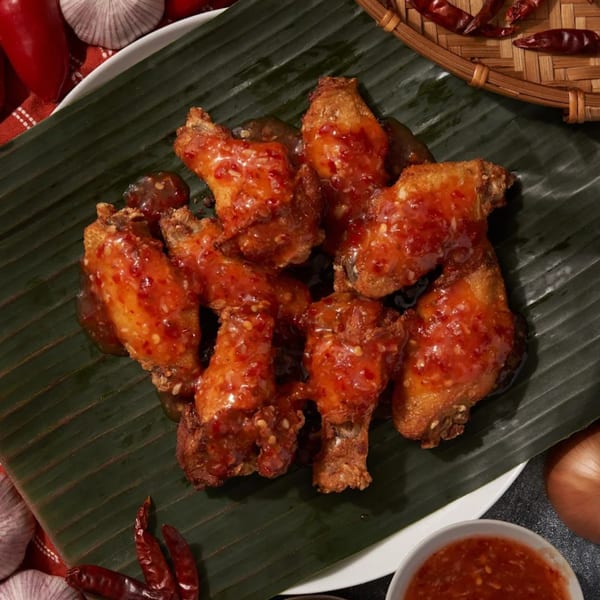 Shlap Muan Chicken Wings, crispy wings coated in sweet chili sauce on a banana leaf.