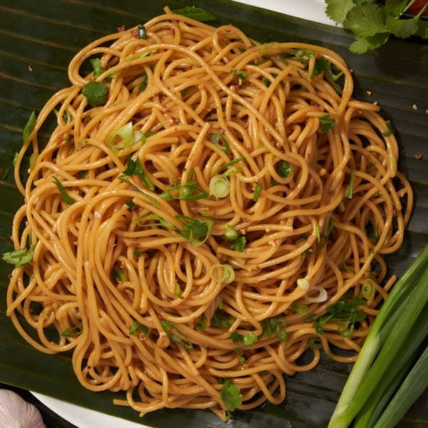 Shlap Muan Chicken Wings' garlic noodles, garnished with green onions and cilantro on a banana leaf.